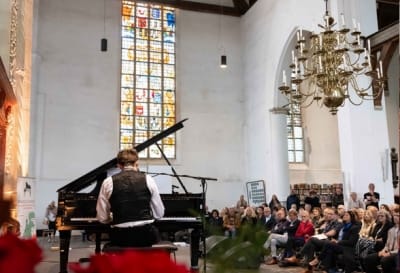 Edam pianowandeling Pianist playing the grand piano during the Pianowalk in Edam (Netherlands) with audience in Grote Kerk